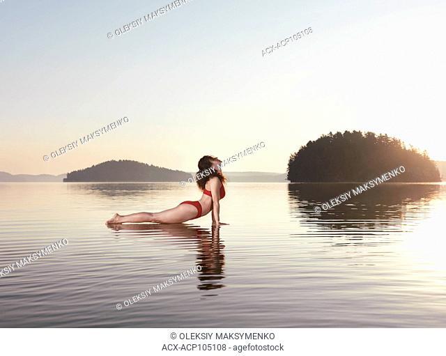 Young woman practicing Hatha yoga on a floating platform in water on the lake during misty sunrise in the morning. Yoga Upward Facing Dog