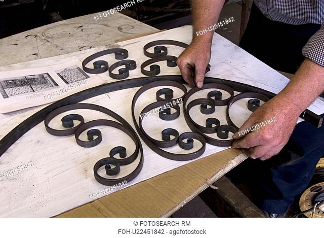 Blacksmith preparing curved top of gate and placing crafted metal scrolls in frame to check for accuracy prior to assembly