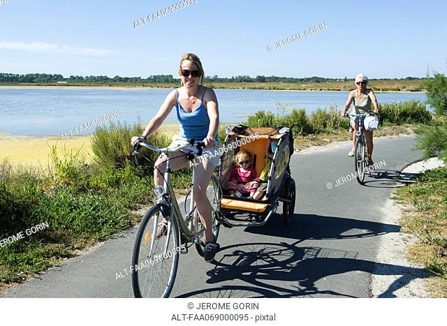 Multi-generation family enjoying bicycle ride, children sitting in bicycle trailer