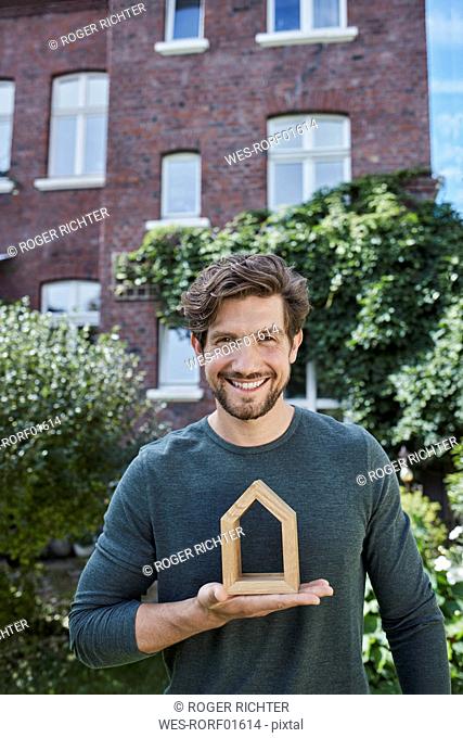 Portrait of smiling man in front of his home holding house model