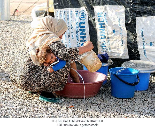 A mother washes her daughter in a bowl with water on the dusty gravel path between the accommodations in the Debaga refugee camp between Mosul and Erbil, Iraq
