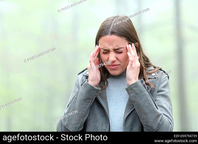 Stressed woman suffering migraine in a cold foggy day in a park