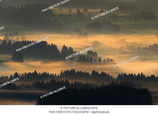15 June 2018, Germany, Eisenberg: The rising sun coloring morning fog rising over the fields. Photo: Karl-Josef Hildenbrand/dpa