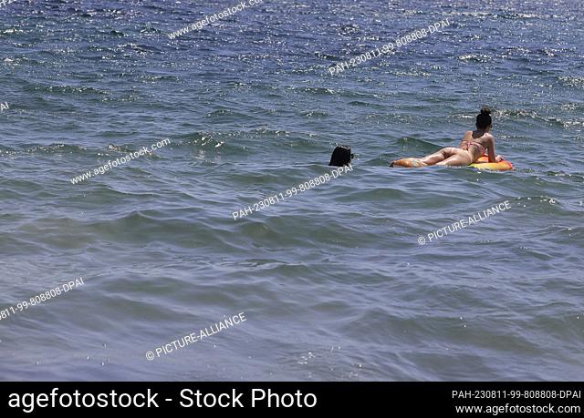 11 August 2023, Spain, Eivissa: Two women are swimming on an inflatable air mattress in the sea near Platja d`en Bossa beach. Photo: Clara Margais/dpa