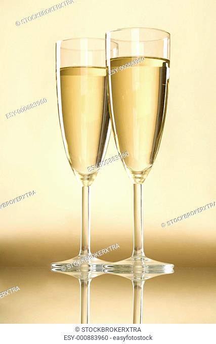 Image of full champagne flutes standing on table with reflection over golden background