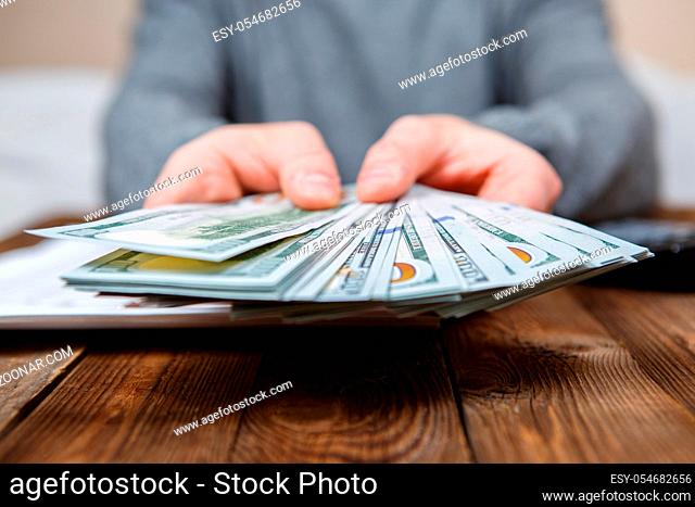 Caucasian hands counting dollar banknotes on dark wooden table
