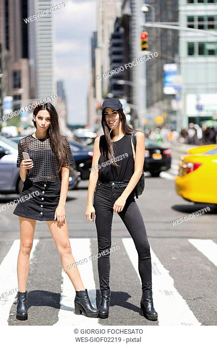 USA, New York City, two fashionable twin sisters standing on zebra crossing in Manhattan