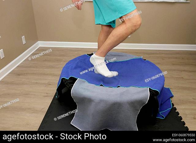 Round bungee rebounder covered with two towels being exercised on close-up on a mat on a floor indoors. Adult male legs and feet stepping