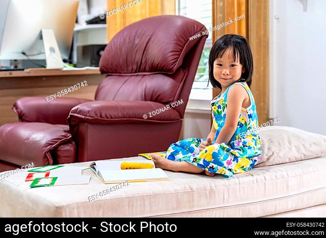 Portrait of Happy asian girl child reading interactive book in living room at home as home schooling while city lockdown because of covid-19 pandemic across the...