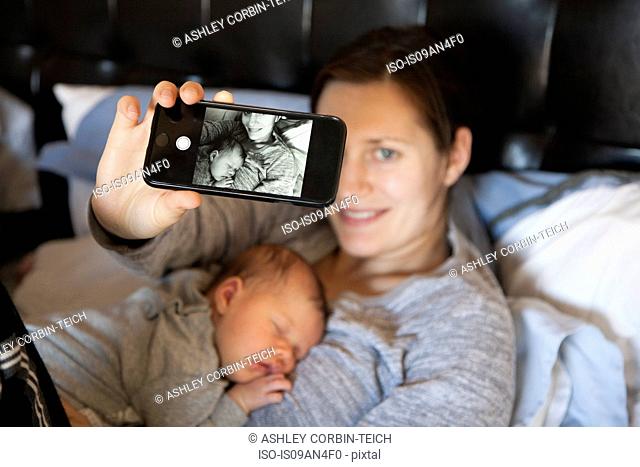 Baby girl sleeping on mother's chest, while mother takes self portrait of them both, using smartphone