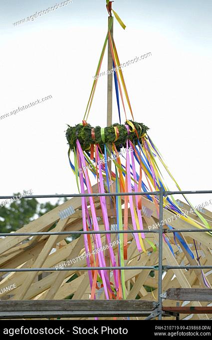 24 June 2021, Saxony, Leipzig: Topping-out wreath on a newly built house. Topping-out ceremony on a gap development. A topping-out wreath hangs from the roof...