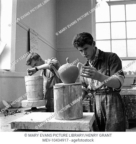 At Stoke College of Art a young student studies a beautiful large teapot which he is making while another works to remove a clay jug from a cast
