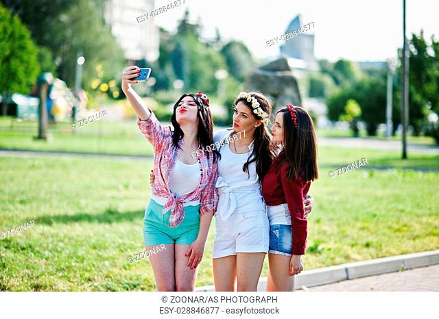 Three girls in short shorts and wreaths on heads make selfie