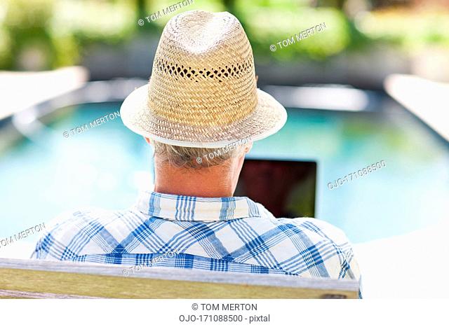 Senior man using laptop at poolside