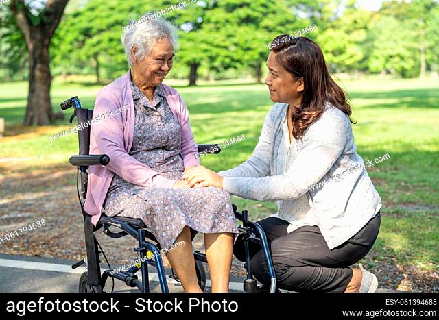 Caregiver help and care Asian senior or elderly old lady woman patient sitting and happy on wheelchair in park, healthy strong medical concept