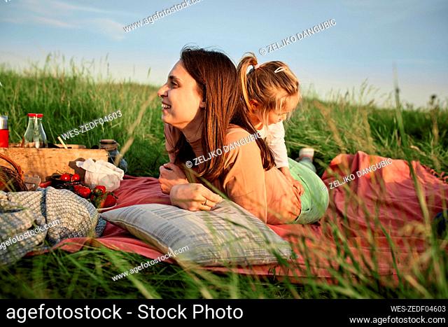 Smiling young woman lying on front by daughter in agricultural field