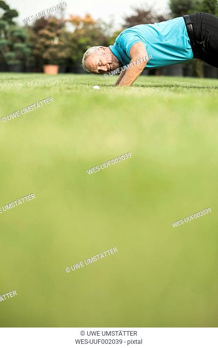 Golf player kneeling on turf looking at golf ball