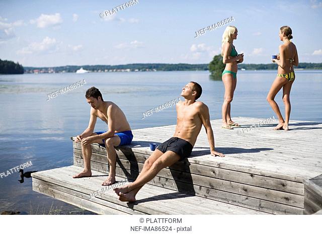Four people relaxing on jetty by lake