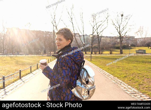 Portrait of smiling woman with backpack and coffee to go in a park, Berlin, Germany