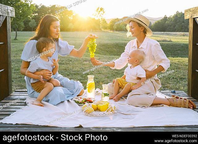 Woman giving grapes to friend sitting on picnic blanket