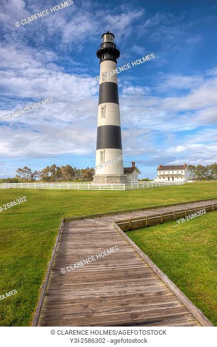 An early morning view of the Bodie Island lighthouse and adjacent boardwalk under a partly cloudy sky in Cape Hatteras National Seashore in the Outer Banks of...