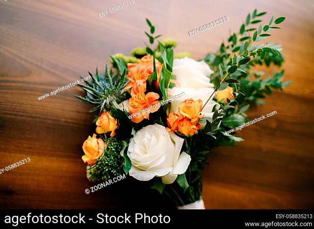 bridal bouquet of white and orange roses, eringyum, ammi, boxwood branches, alstroemeria with white ribbons on the floor. High quality photo