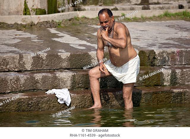 Indian Hindu man bathing and cleaning his teeth in the River Ganges by Kshameshwar Ghat in holy city of Varanasi, India