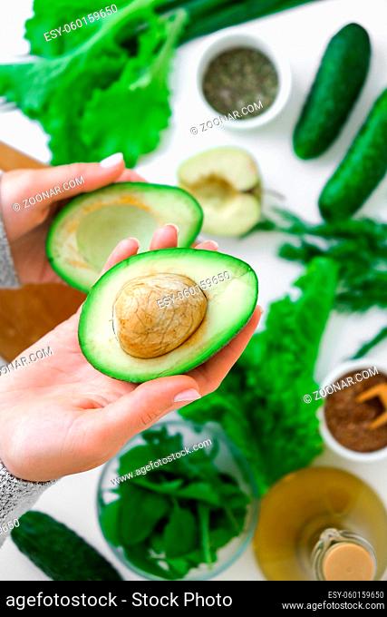 Woman cooking salad of fresh green vegetables and herbs. Cooking healthy diet or vegetarian food. Female hands hold avocado surrounded by green vegetables