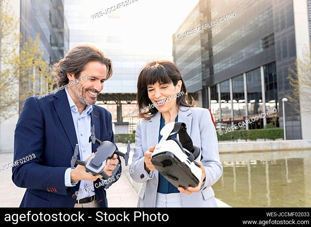 Smiling male and female professionals holding drone and virtual reality headset in park