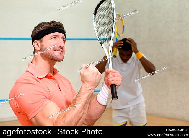 Cute men playing squash. Hansome muscular man in orange t-shirt expressing astonishment and excitedness after great battle in squash