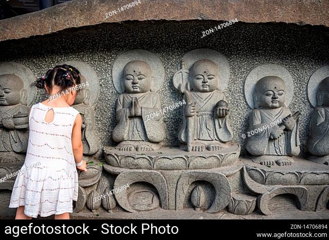 Chengdu, China - July 2019 : Little Chinese girl in a white dress leaving flowers under the small holy sculptures in Wenshu Monastery