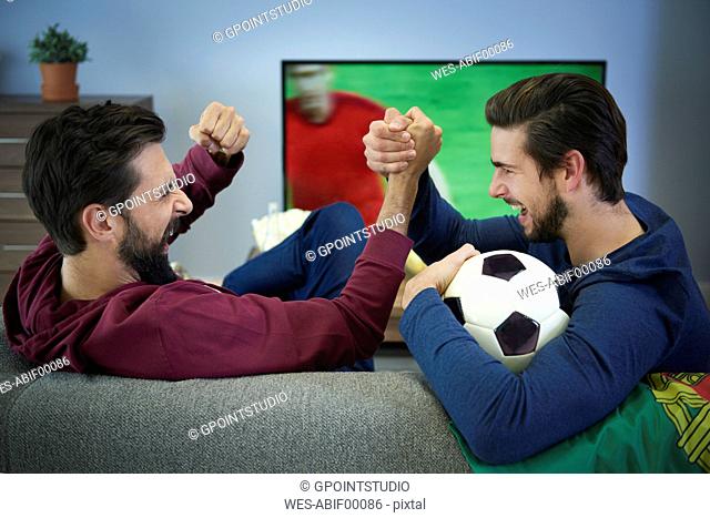 Two football fans watching Tv and cheering
