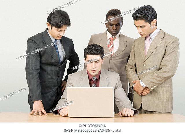 Three businessmen looking at their colleague using a laptop