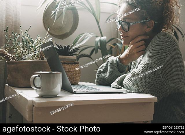 Serene woman work with notebook at home smiling at the display. Serene female use laptop indoor with plants in background