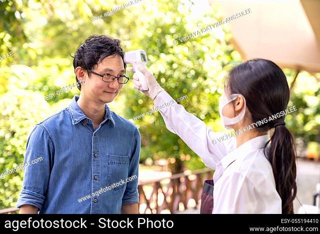 Asian waitress with face mask take temperature customer before getting in restaurant. Restaurant New normal restaurant lifestyle concept after coronavirus...
