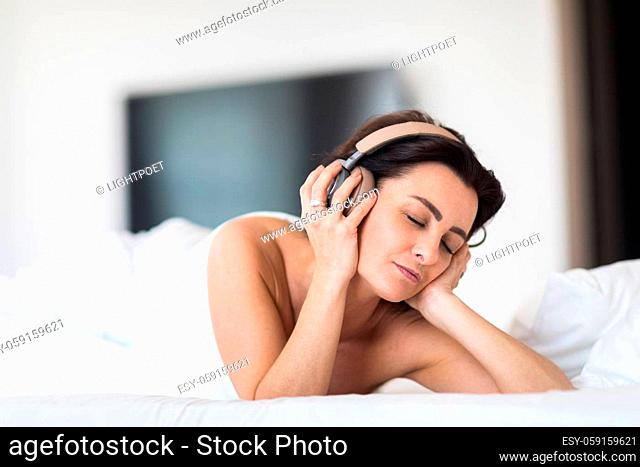 Pretty, young woman listening to music on her hi-fi headphones in bed, relaxing