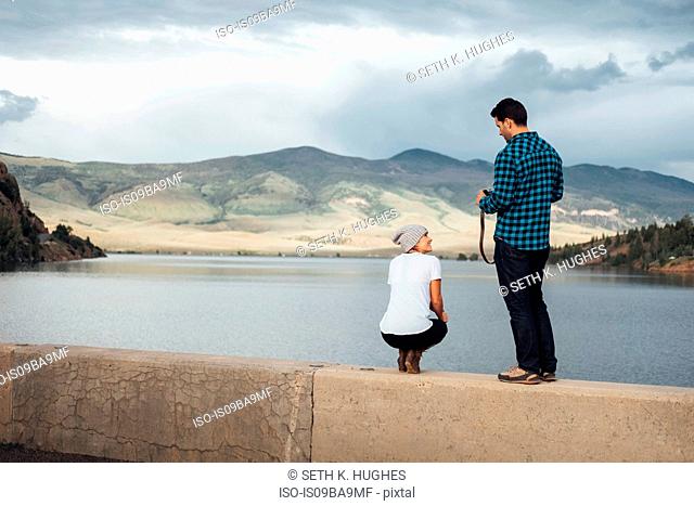 Couple on wall beside Dillon Reservoir, man holding camera, rear view, Silverthorne, Colorado, USA