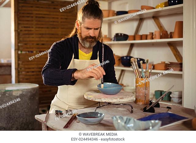 Attentive male potter painting on bowl