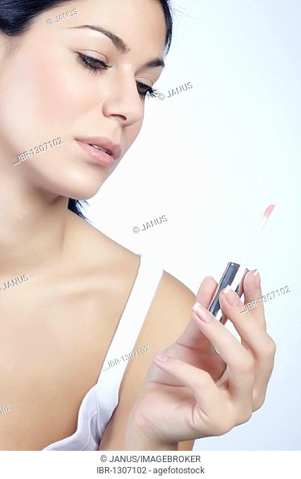Young woman looking at her lip gloss in her hand, beauty