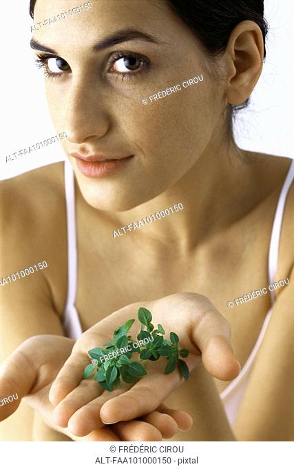 Young woman holding out handful of fresh thyme, looking at camera