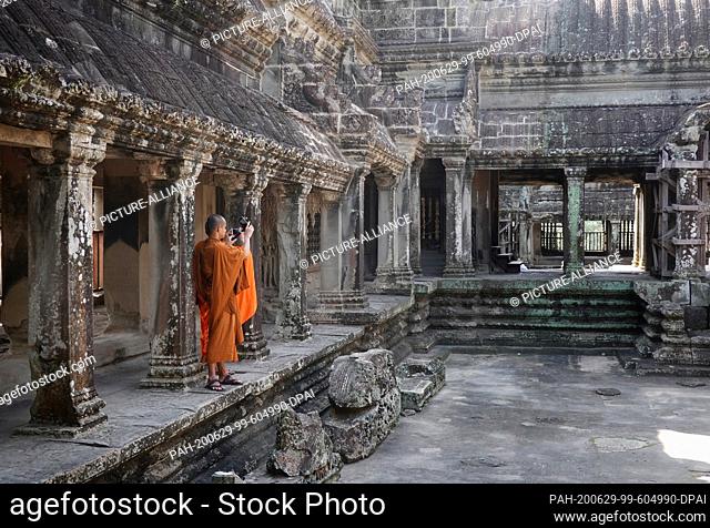 23 October 2019, Cambodia, Siem Reab: A monk in an orange cloak takes photos in the main temple Angkor Wat. King Suryavarman had the temple