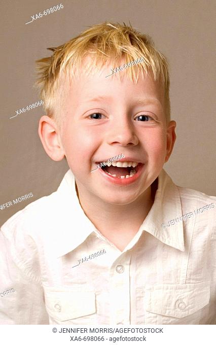 A five-year-old blonde-haired, blue eyed boy is laughing and looking straight at the camera. He is wearing a white shirt and one of his teeth is missing