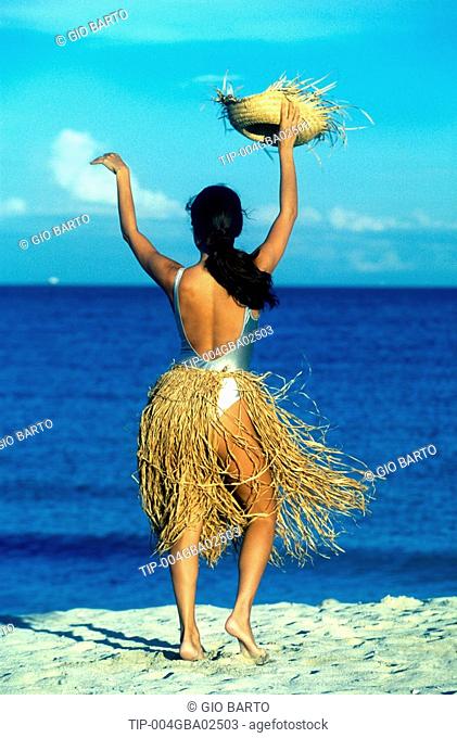 Woman with straw skirt and hat, dancing on a beach