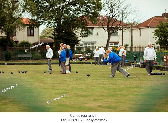 A side view shot of a senior woman taking her shot in a game of lawn bowling, surrounded by other seniors in the community