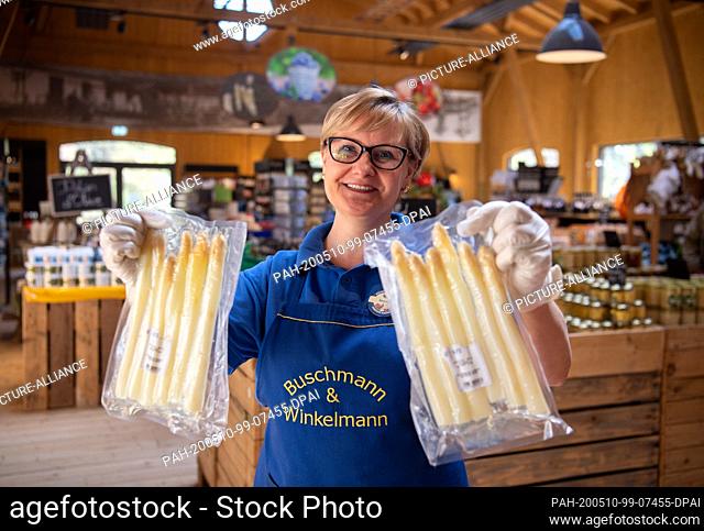 21 April 2020, Brandenburg, Klaistow: Saleswoman Iwona shows two packets of pre-cooked fresh asparagus in the farm shop. The pre-cooked food has been available...