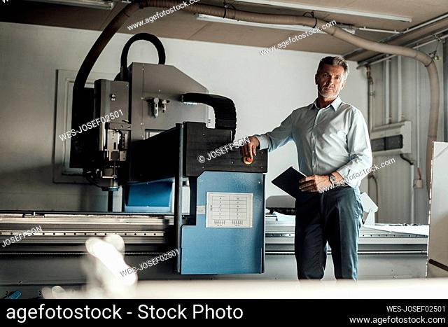 Male engineer with digital tablet standing by manufacturing equipment in factory
