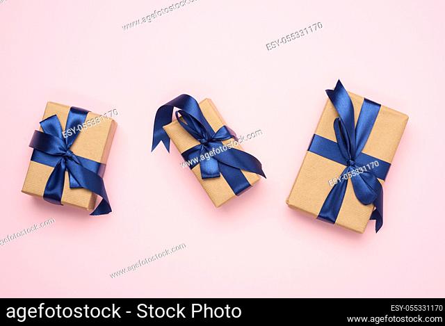 rectangular box wrapped in brown paper and tied with a blue silk ribbon with a bow, gift on a pink background, top view, copy space