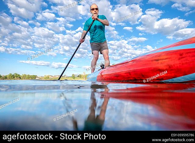Senior male paddling a stand up paddleboard on a calm lake in Colorado - low angle view from action camera. Recreation, training and fitness concept