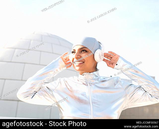 Smiling woman wearing protective suit listening music while standing against igloo