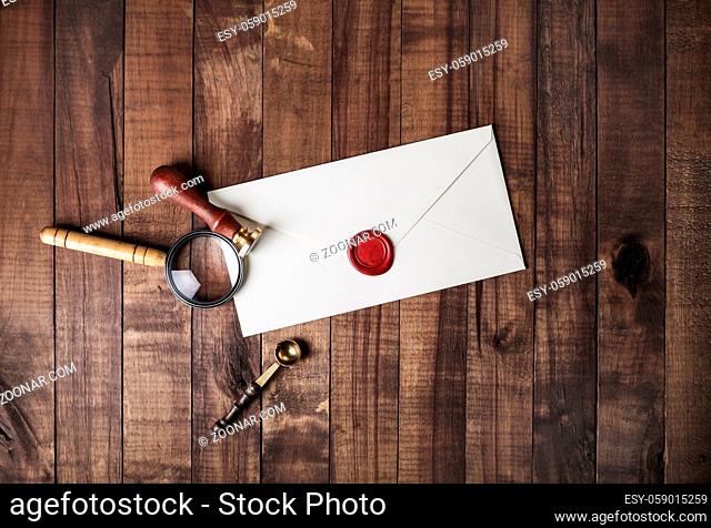 Blank paper envelope with red wax seal, stamp, spoon and magnifier on wooden background. Mockup for your design. Flat lay